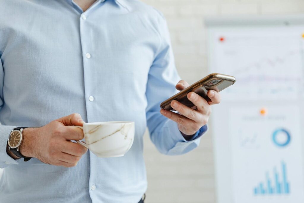 A person wearing a blue shirt holding a phone and a cup behind a chart
