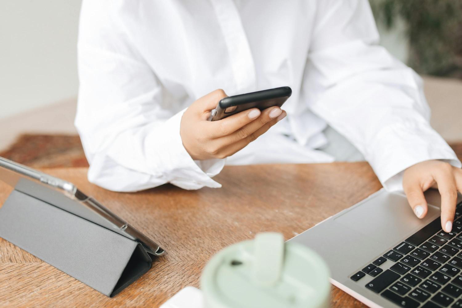 A person in a white shirt using a smartphone and a laptop