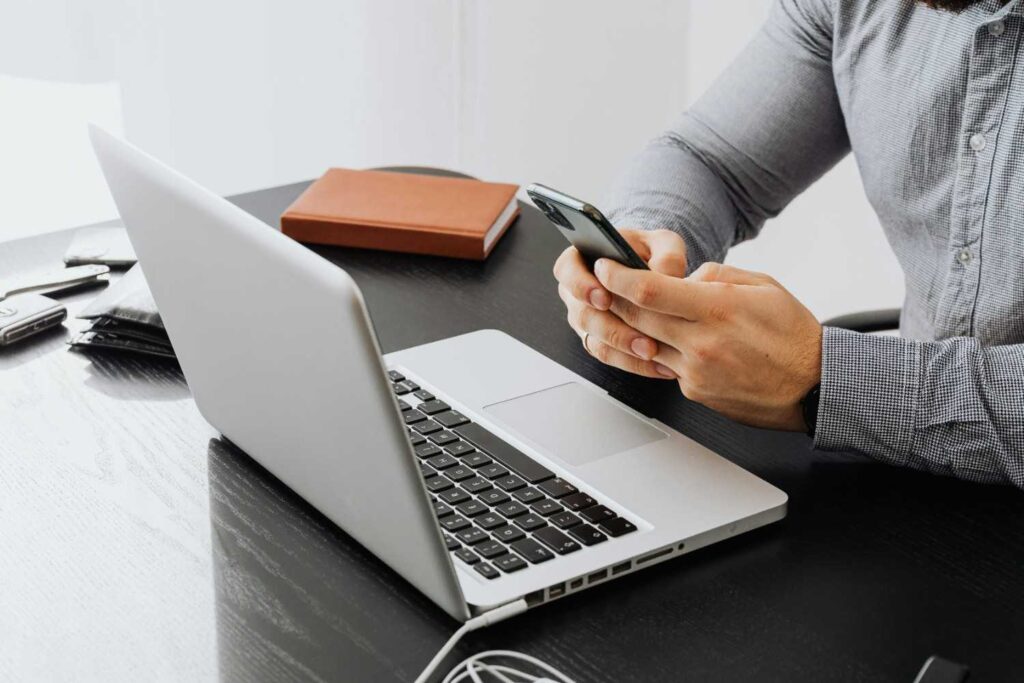 Seorang menggunakan komputer riba dan telefon di atas meja